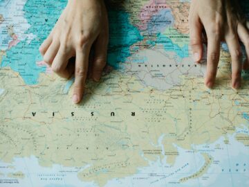 Close-up of hands pointing at Russia on a detailed world map.