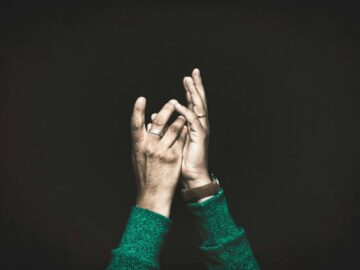 Close-up of hands clapping on a dark background, with visible rings and wristwatch.