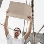 A man holds a blank sign on the iconic Brooklyn Bridge, ready for customization.