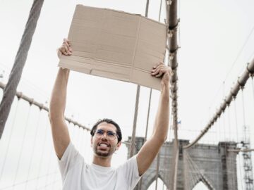A man holds a blank sign on the iconic Brooklyn Bridge, ready for customization.
