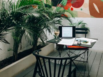 Stylish outdoor workspace with a laptop, documents, and coffee in a vibrant garden patio setting.