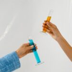 Two hands holding orange and blue liquid in test tubes, symbolizing research.
