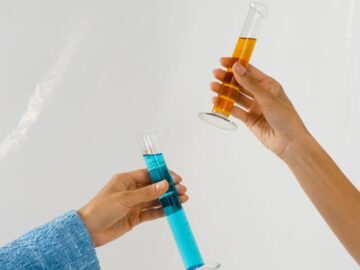 Two hands holding orange and blue liquid in test tubes, symbolizing research.
