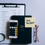 Top view of a desk with income statement, phone calculator, and tax reminder note.