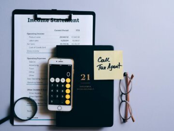 Top view of a desk with income statement, phone calculator, and tax reminder note.