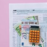 A vibrant flat lay of a calculator, euro banknotes, and US tax forms on a pink background.