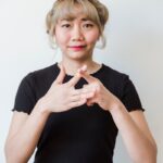 Portrait of an Asian woman using sign language in front of a white background, smiling warmly.