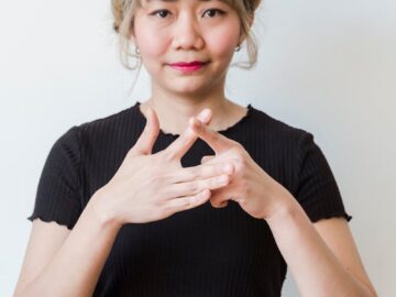 Portrait of an Asian woman using sign language in front of a white background, smiling warmly.