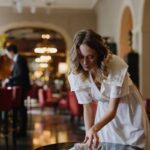 Elegant waitress cleaning a table in a luxurious restaurant interior with warm lighting.