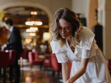 Elegant waitress cleaning a table in a luxurious restaurant interior with warm lighting.
