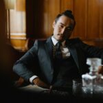 Elegant man in formal attire seated in a classic wood-paneled lounge, exuding sophistication.