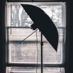 Silhouette of a photography umbrella against a window with blinds, creating an artistic contrast.