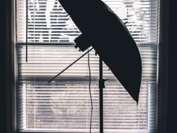Silhouette of a photography umbrella against a window with blinds, creating an artistic contrast.