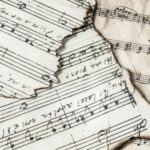 Close-up of aged, burnt music sheets displaying musical notes and compositions in detail.