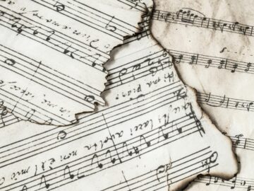 Close-up of aged, burnt music sheets displaying musical notes and compositions in detail.