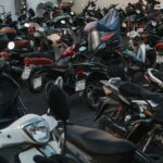 A packed parking area filled with various parked motorcycles during the evening.