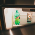A green soda bottle and a beverage in an open fridge, showcasing indoor lighting and storage.