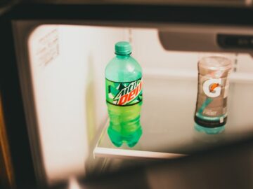 A green soda bottle and a beverage in an open fridge, showcasing indoor lighting and storage.