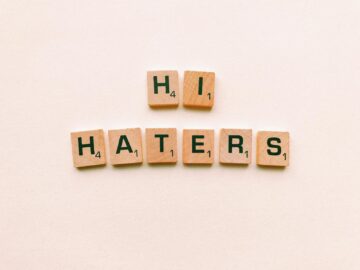 Wooden scrabble tiles spelling 'Hi Haters' on a light beige background.
