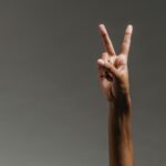 Close-up image of a hand making a peace sign against a neutral background.