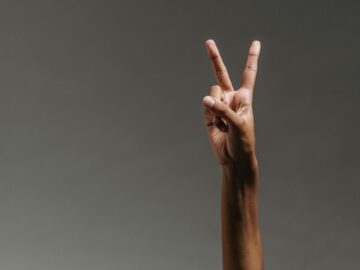 Close-up image of a hand making a peace sign against a neutral background.