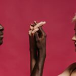A close-up of an interracial couple holding hands against a pink background, symbolizing unity.