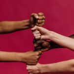 Close-up of diverse hands forming fists, symbolizing unity and teamwork on a vivid pink background.