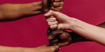 Close-up of diverse hands forming fists, symbolizing unity and teamwork on a vivid pink background.