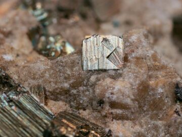 Detailed close-up of pyrite crystal on rocky surface, showcasing natural textures and colors.