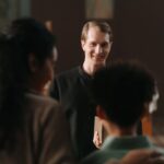 A smiling priest engages with parishioners in a church environment, exuding warmth and connection.