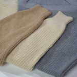 A collection of folded knit sweaters in earthy tones displayed in a flat lay arrangement.