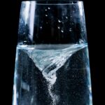 Close-up of a mesmerizing water vortex in a glass with droplets against a dark background.
