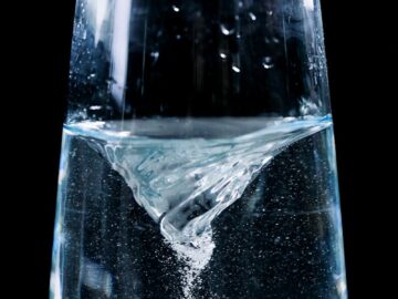 Close-up of a mesmerizing water vortex in a glass with droplets against a dark background.