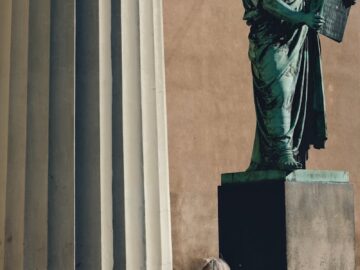 Woman reading in sunlight next to a grand stone statue and column.