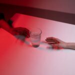 Two diverse hands reaching towards a glass of water on a table with dramatic red lighting.