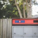 A Canada Post mailbox with colorful label outdoors with trees in the background.