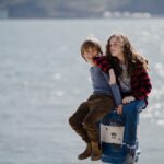 woman and child sits on white and blue metal capstan in dock