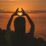 silhouette of woman doing heart sign during sunset