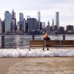 person in knit cap sitting on wooden bench in front of body of water during daytime