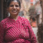 woman wearing red and grey long-sleeved floral dress smiling between buildings