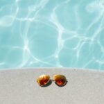 gold framed orange lens Aviator-style sunglasses beside pool