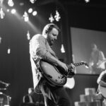 greyscale photo of man playing electric guitar on stage