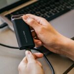 A person holding an external hard drive in front of a laptop