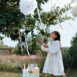 A young girl in a white dress enjoys a festive garden party with decorations and fresh lemonade.