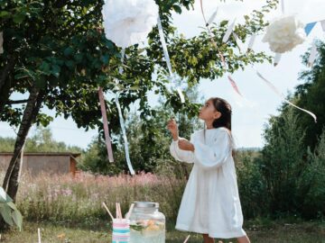 A young girl in a white dress enjoys a festive garden party with decorations and fresh lemonade.