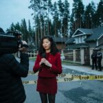 Journalist reporting live from a taped crime scene with cameraman and police.