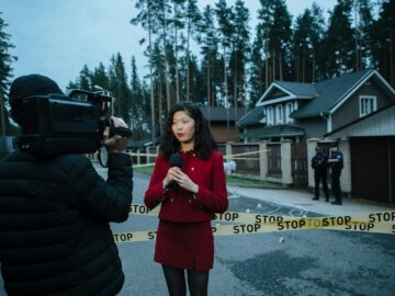 Journalist reporting live from a taped crime scene with cameraman and police.