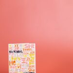 A vibrant display featuring pronouns card and rainbow 'human' sign against a red studio background.