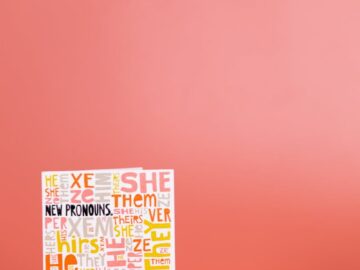 A vibrant display featuring pronouns card and rainbow 'human' sign against a red studio background.