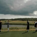 Four women maintaining social distance in a dramatic, cloudy outdoor setting.